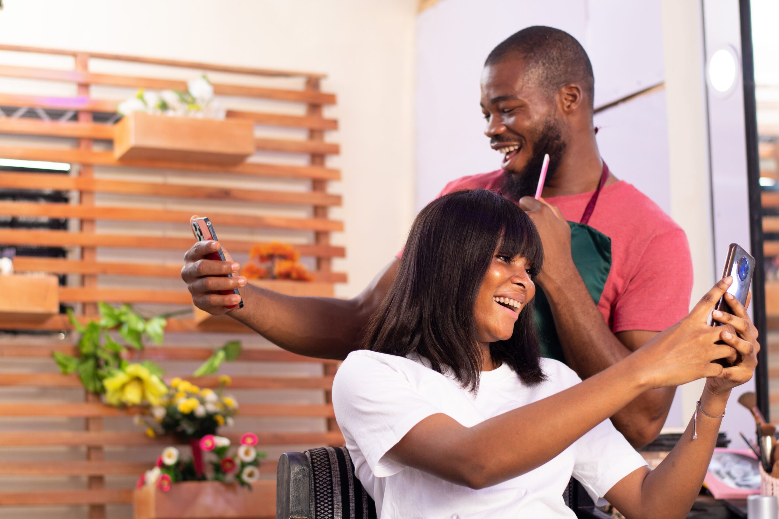 nigerian man and woman in a hair salon holding their phones and smiling